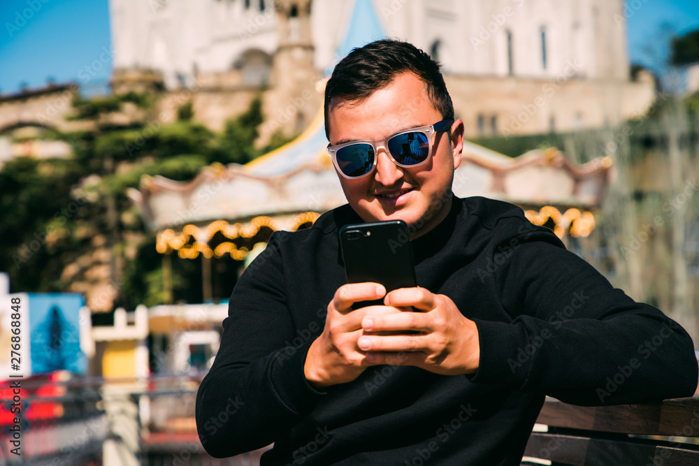 Young handsome man in sunglasses use phone while sitting on the bench. Summer vocation. Young handsome man in sunglasses use phone while sitting on the bench. Summer vocation.