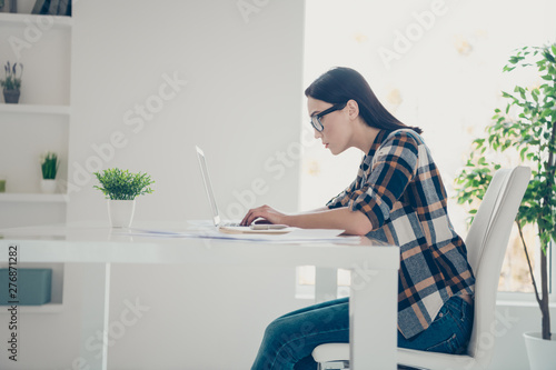 Profile side view photo concentrated pensive entrepreneur modern technology device look screen sit chair white trendy stylish she her eyewear eyeglasses checkered shirt denim plaid jeans apartment