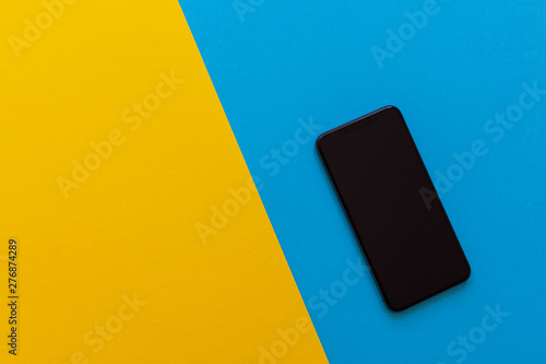 New modern black phone on yellow and blue background, flat lay, copy space