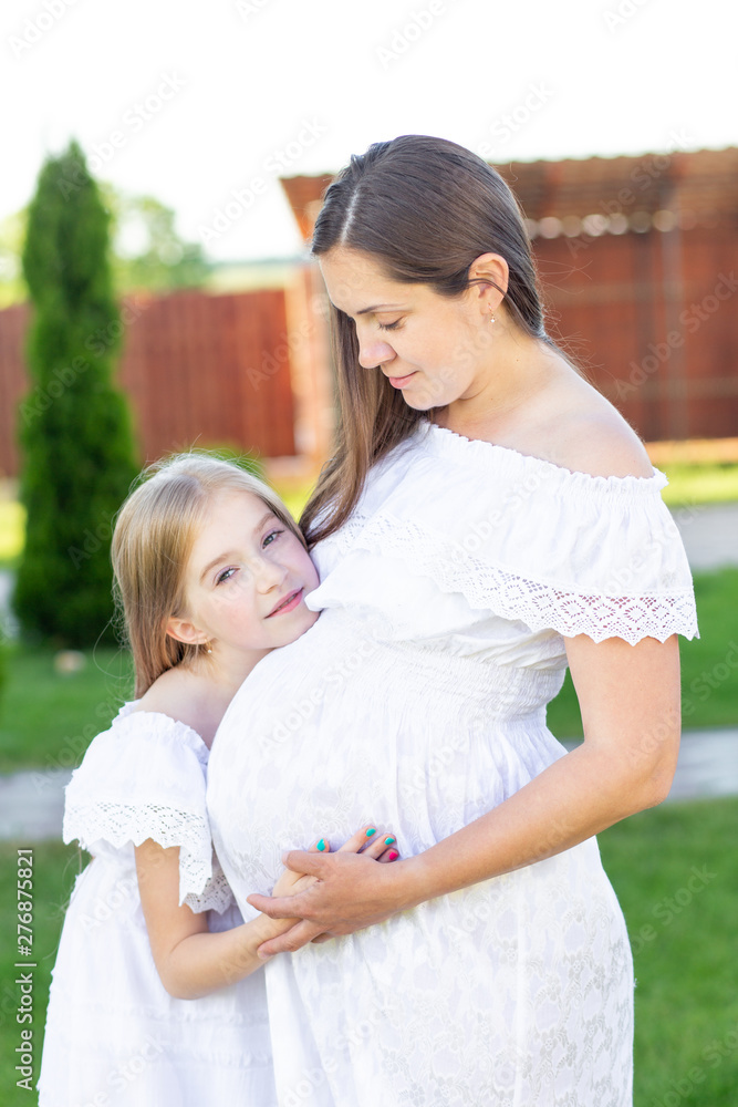 Pregnant mom and daughter are resting in nature. Long-haired girls in white dresses. Pregnant girl with long hair Pregnant mom and daughter are resting in nature. Long-haired girls in white dresses. Pregnant girl with long hair
