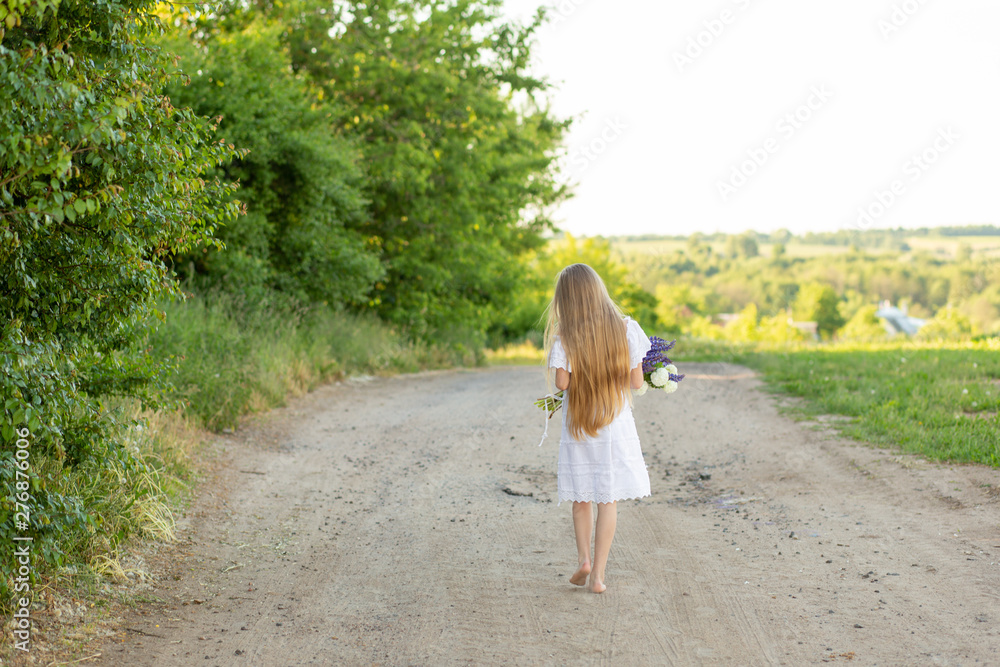 Beautiful young girl with long blond hair with a bouquet in her hands. Girl walking in the countryside