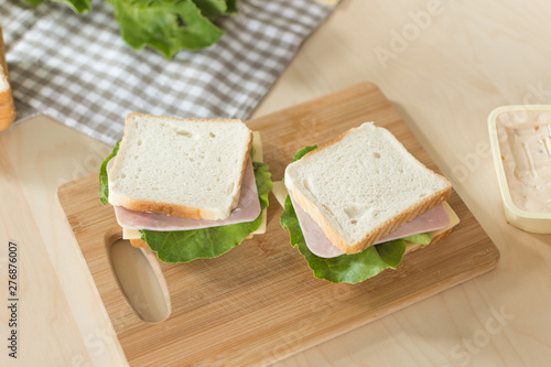 Sandwich with cheese and ham on cutting board on the table in the bright kitchen. Lunch. Sandwich with lettuce. Healthy eating concept.