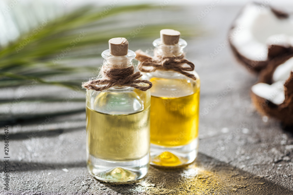 selective focus of bottles with coconut oil near green palm leaf and cracked coconut selective focus of bottles with coconut oil near green palm leaf and cracked coconut