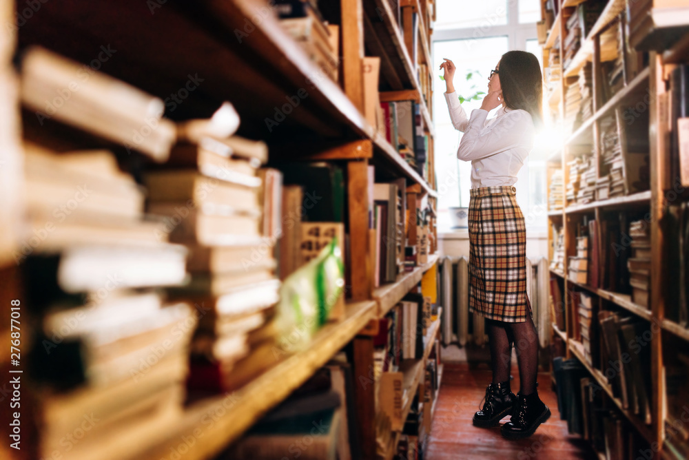 people, knowledge, education and school concept - student girl select a book on the shelf in the old library people, knowledge, education and school concept - student girl select a book on the shelf in the old library