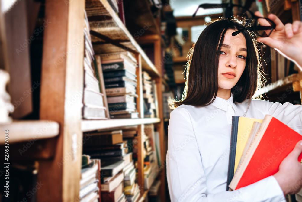 people, knowledge, education and school concept - happy student girl or young woman with book posing in an old library people, knowledge, education and school concept - happy student girl or young woman with book posing in an old library