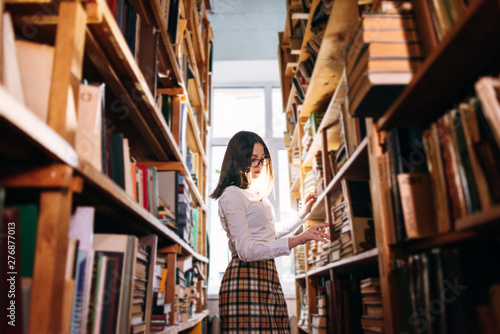 people, knowledge, education and school concept - student girl select a book on the shelf in the old library