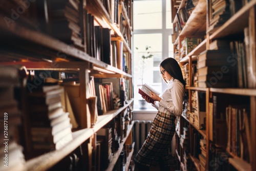 people, knowledge, education and school concept - student girl or young woman reading a book in the old library