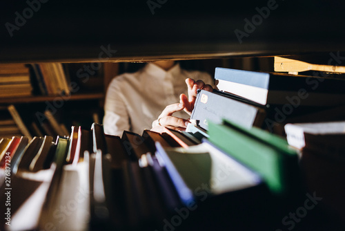 people, knowledge, education and school concept - student girl select a book on the shelf in the old library