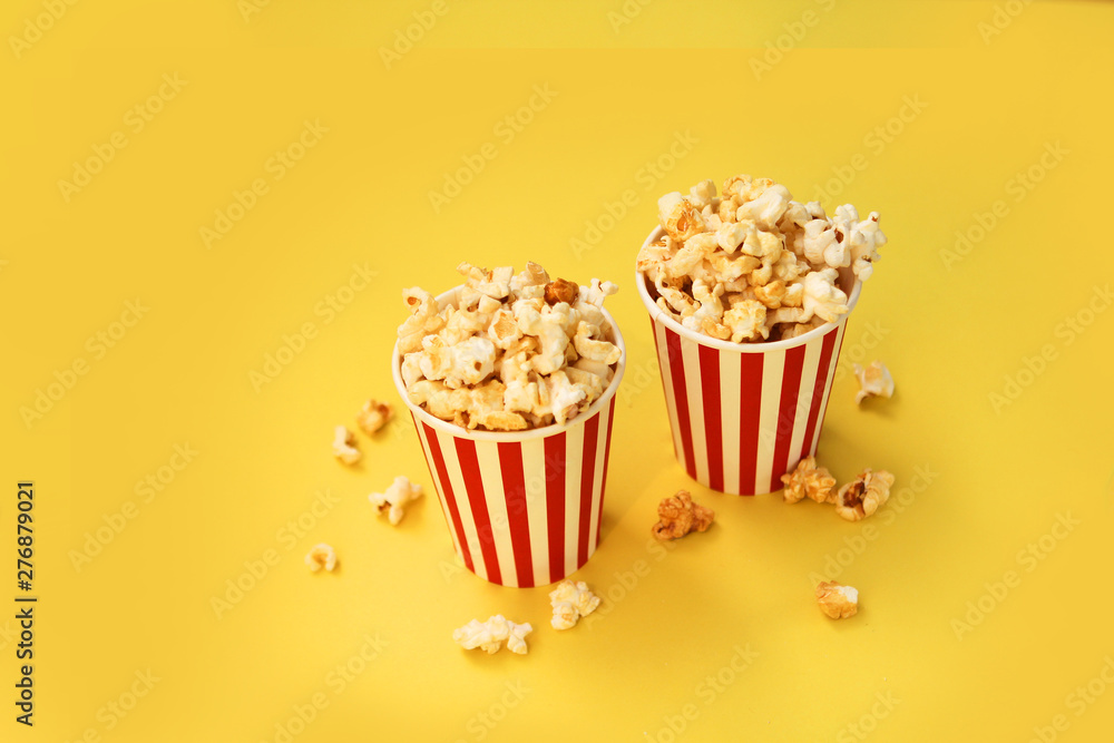 two red-white paper cups with popcorn on a yellow background, several pieces are scattered nearby, copy space