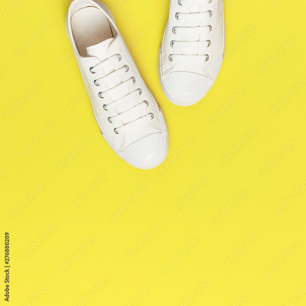 White female fashion sneakers on yellow background. Flat lay top view copy space. Women's shoes. Stylish white sneakers. Fashion blog or magazine concept. Minimalistic shoe background, sport White female fashion sneakers on yellow background. Flat lay top view copy space. Women's shoes. Stylish white sneakers. Fashion blog or magazine concept. Minimalistic shoe background, sport