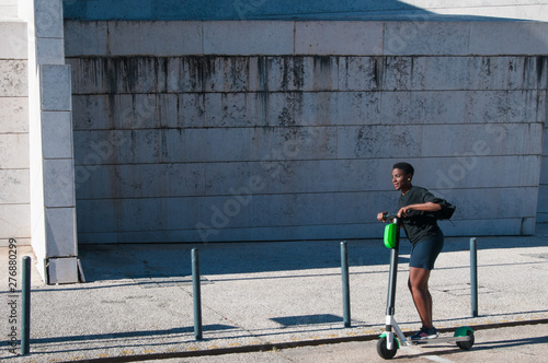 Positive black woman riding electric scooter outdoors. Young woman wearing casual blouse and skirt with building in background. Modern transportation concept.