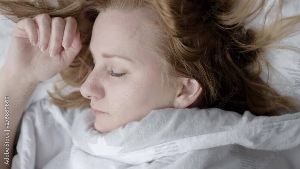 Beautiful young girl is sleeping on pillow. She is waking up, stretching and smiling. Caucasian woman on bed after waking up early in morning.