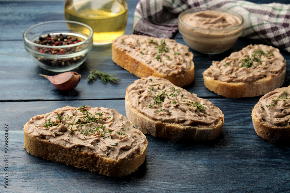 Fresh homemade chicken liver pate with herbs on bread on a blue wooden table. A sandwich.