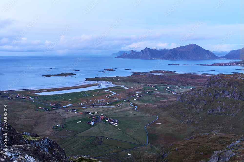 View from above over a bay with snowcapped mountains during evening blue hour on Lofoten Islands in Norway.