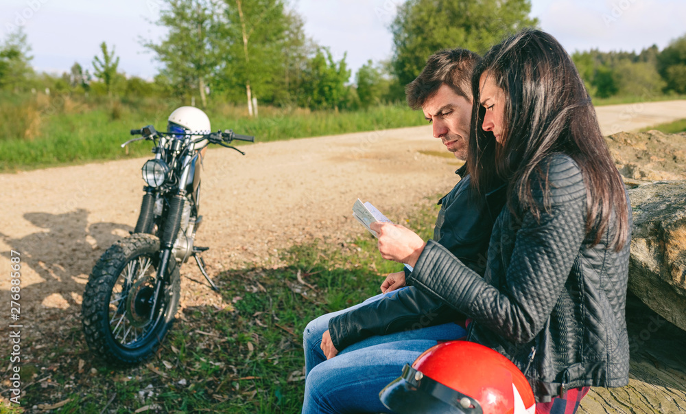 Lost young couple sitting looking at a map during a motorcycle trip Lost young couple sitting looking at a map during a motorcycle trip