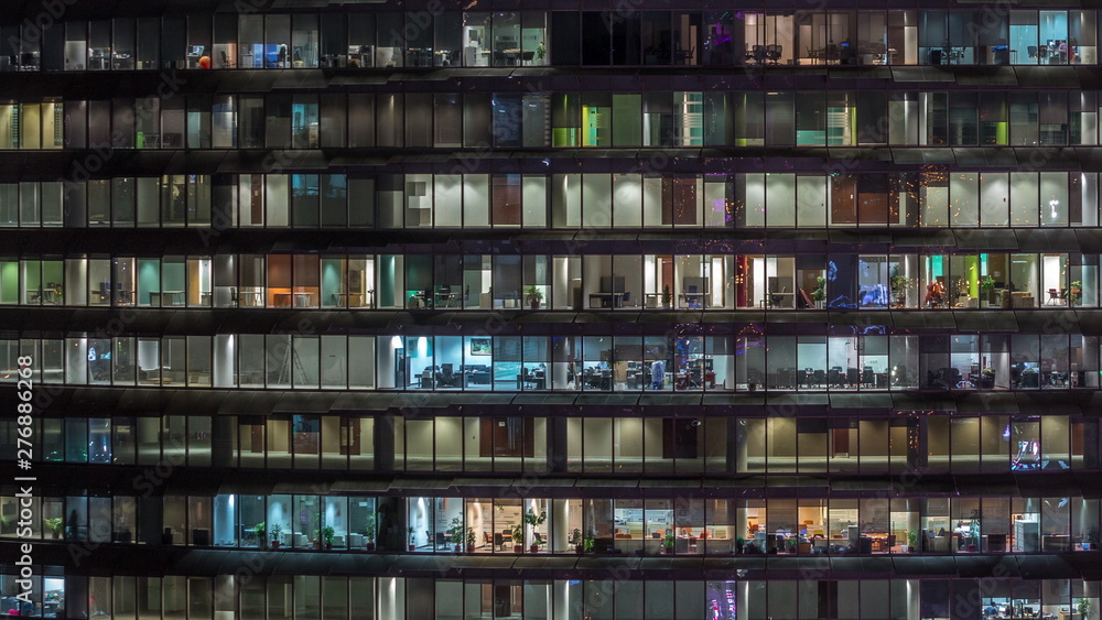 Working evening in glass office building with numerous offices with glass walls and windows timelapse