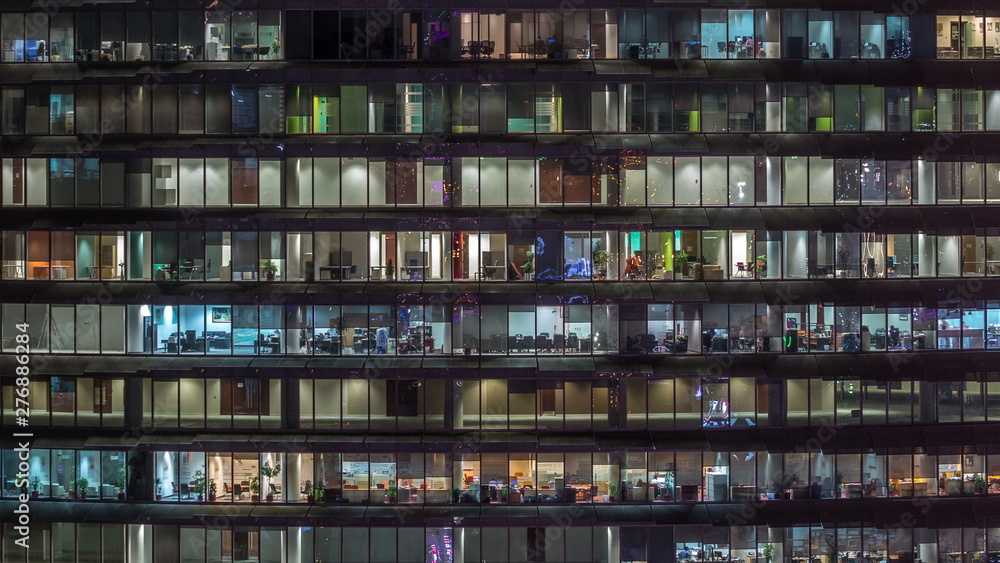 Working evening in glass office building with numerous offices with glass walls and windows timelapse