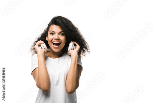 pretty african american girl holding headphones while looking at camera isolated on white