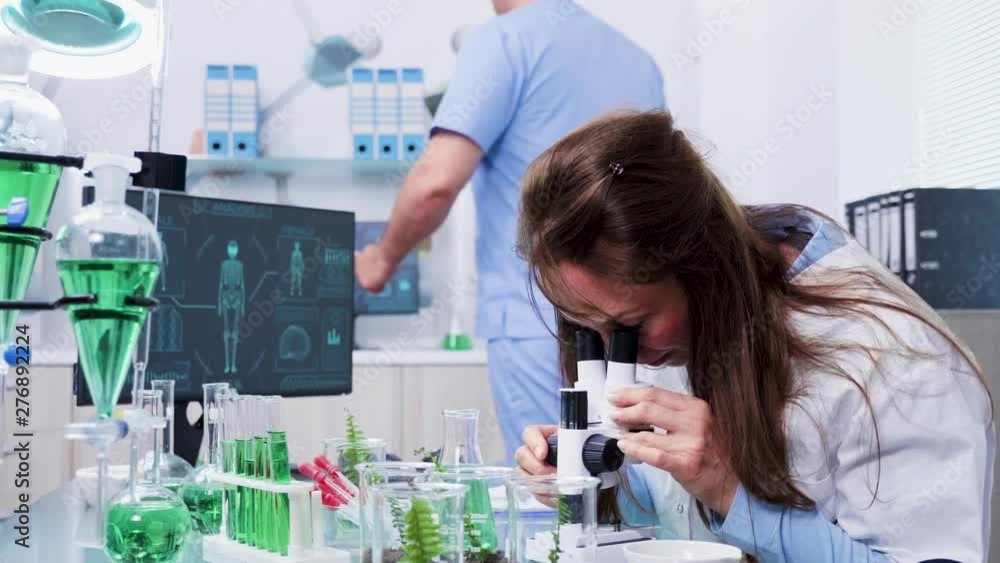 Revealing shot of female scientist looking into the microscope in modern laboratory Revealing shot of female scientist looking into the microscope in modern laboratory