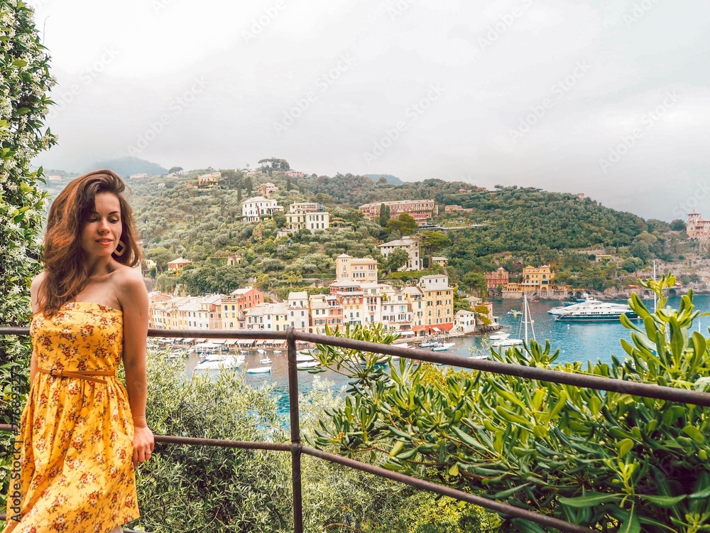 Brunette girl with long hair in a bright summer yellow dress on the background of colorful houses and yachts in the Bay in Portofino, Liguria, Italy