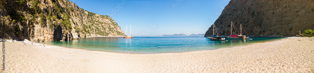 Sailing ships moored in a secluded bay with turquoise water and empty beach at sunrise, Oludeniz, Turkey panoramic