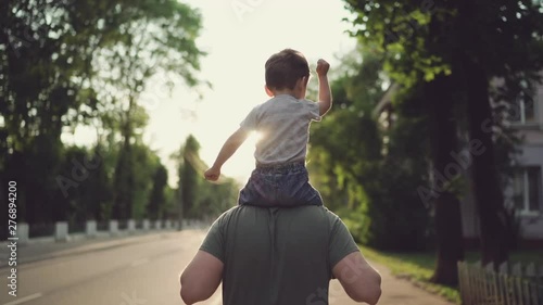 Father and son walking in city at sunset, Two year old kid is sitting on the parent's shoulders photo