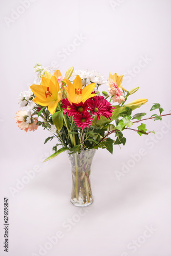 Ramo de flores colorido en un jarrón de cristal sobre fondo blanco, con margaritas, gerberas y lirios.
