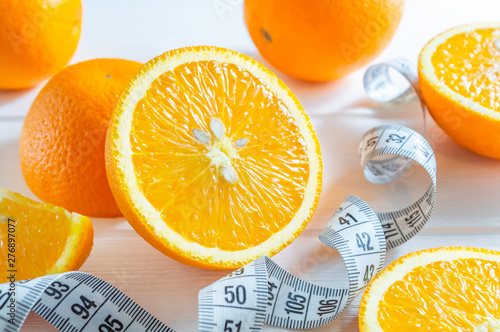 Fresh sliced and whole oranges, and measuring tape on white wooden table.