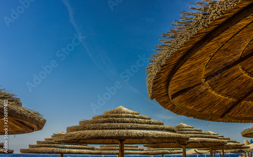 straw umbrellas on a beach coast line photography foreshortening from below on vivid blue sky background with empty copy space for text in summer warm vacation season time 