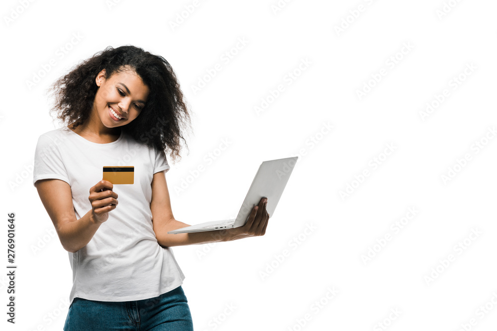 cheerful african american woman holding credit card near laptop isolated on white cheerful african american woman holding credit card near laptop isolated on white