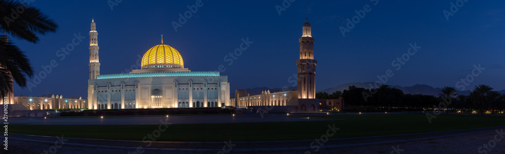 A Panorama of the Sultan Qaboos Grand Mosque in Muscat, Oman in the early evening hour showing off the dark blue sky and glowing dome. 