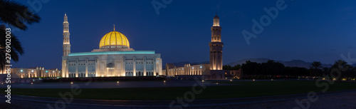 A Panorama of the Sultan Qaboos Grand Mosque in Muscat, Oman in the early evening hour showing off the dark blue sky and glowing dome. 
