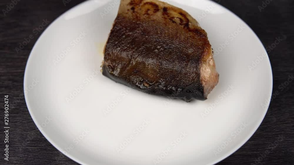 Closeup of cook's hands putting a piece of fried red fish on a white plate on a black background. Closeup of cook's hands putting a piece of fried red fish on a white plate on a black background.