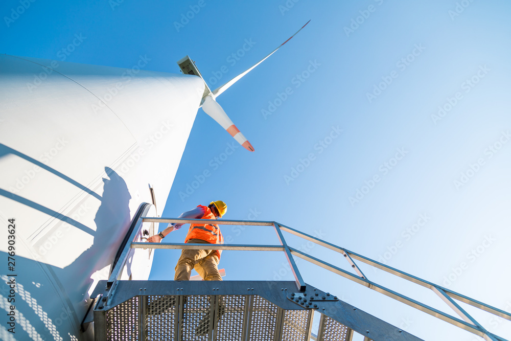 Φωτογραφία Ingegnere con gilet e caschetto fa manutenzione alla turbina eolica alta 100 met