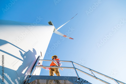 Ingegnere con gilet e caschetto fa manutenzione alla turbina eolica alta 100 metri, in montagna photo