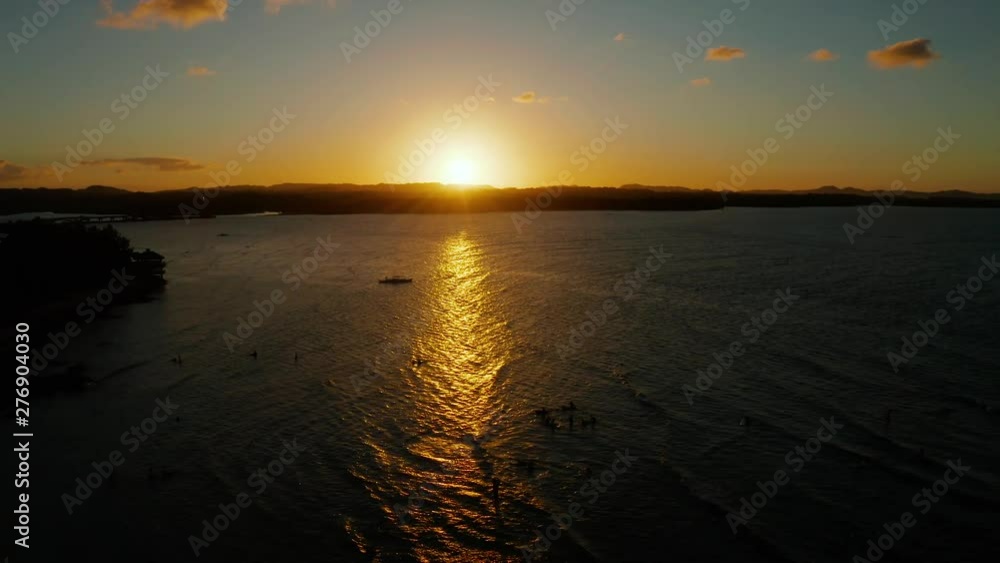 Sunset above the sea with waves and surfers, aerial view. Reflected sun on a water surface. Siargao, Philippines. Sunset over ocean. Sunset above the sea with waves and surfers, aerial view. Reflected sun on a water surface. Siargao, Philippines. Sunset over ocean.
