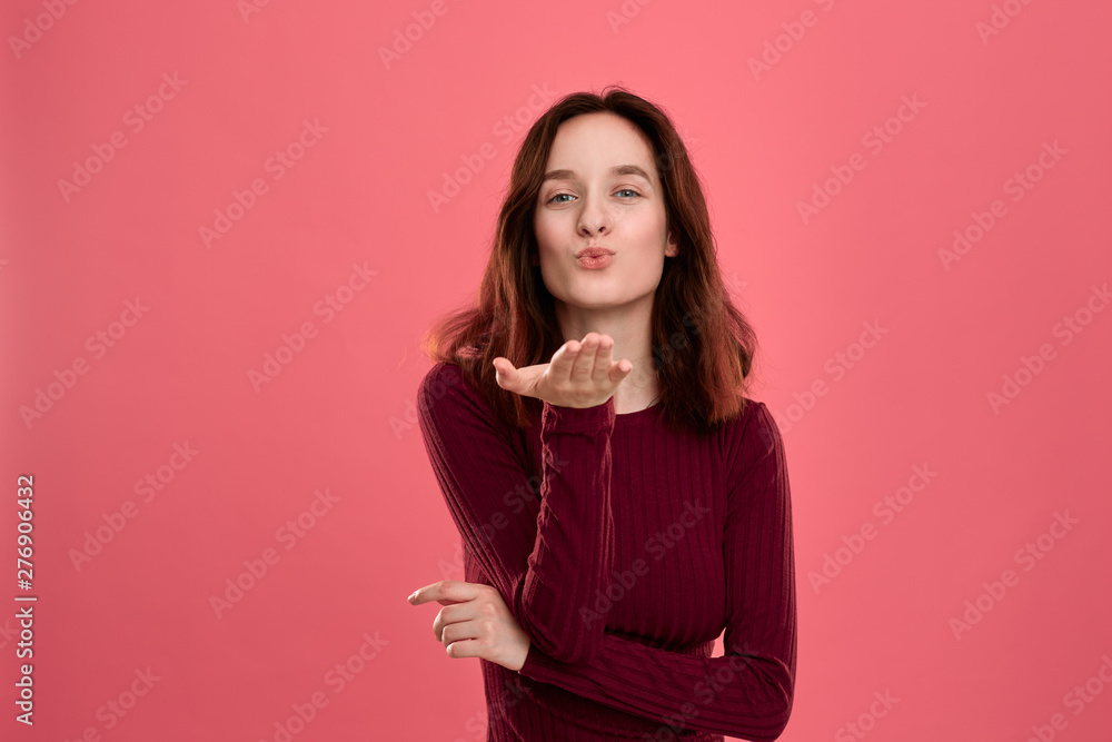 Happy young lady standing isolated over dark pink background while sending romantic hand kisses. Happy young lady standing isolated over dark pink background while sending romantic hand kisses.