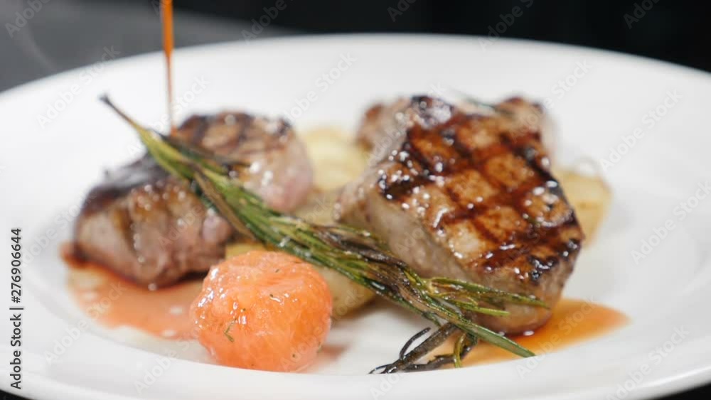 Slow motion food video. Sauce being poured on steak. Grilled meat and potato. Closeup shot of hef pouring sauce over dish with delicious meat on white plate. Food preparation in modern restaurant Slow motion food video. Sauce being poured on steak. Grilled meat and potato. Closeup shot of hef pouring sauce over dish with delicious meat on white plate. Food preparation in modern restaurant