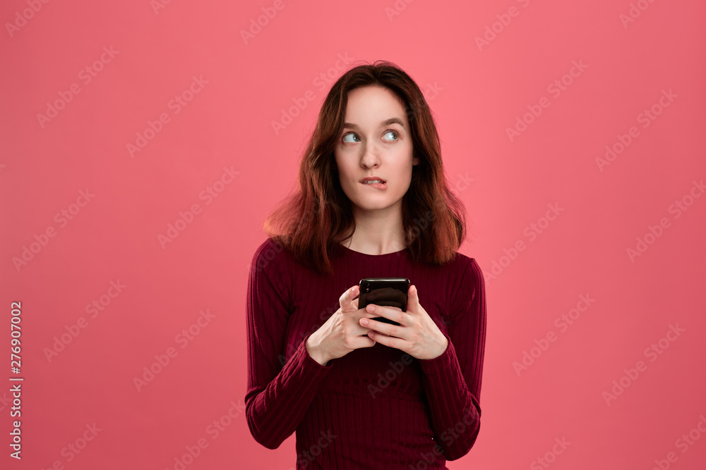 Portrait of a pretty brunette girl standing on a dark pink background and texting on the phone. Portrait of a pretty brunette girl standing on a dark pink background and texting on the phone.