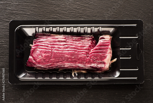 Raw Marbled Beef Bacon vacuum packed on black slate background, top view photo