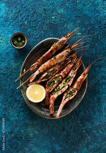 Seafood Shrimps Prawns skewers with garlic and fresh herbs on a blue background, top view. Barbecue srimps prawns photo