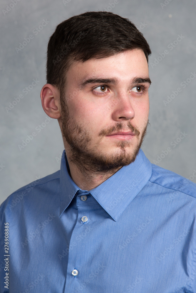 Handsome young stylish man standing in blue shirt in interior on gray background Handsome young stylish man standing in blue shirt in interior on gray background