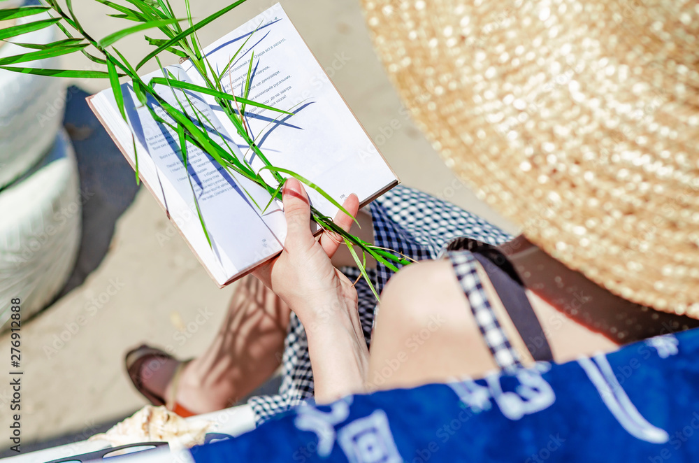 Fototapeta premium Girl in a straw hat reads a book on a bench
