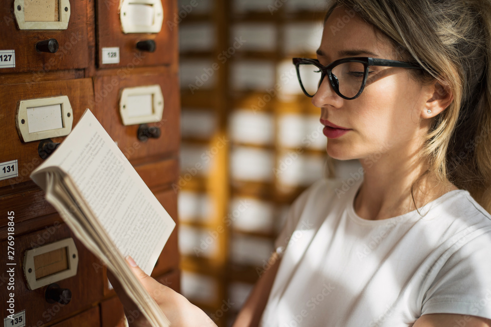 Fototapeta premium Blonde woman reading a book in public library