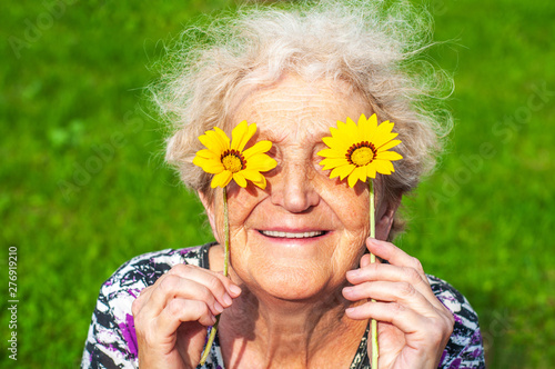 A cheerful grandmother looks at the flower look of yellow daisies. Women's health, skin care, eyesight, sunburn, healthy teeth, wrinkles in old age