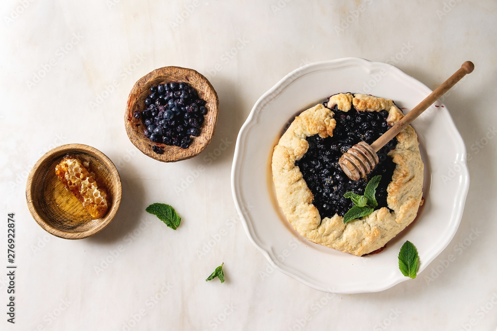 Home baking summer berry biscuit pie with blueberries, served in plate with bowl of blueberry and honey over white marble background. Flat lay, space Home baking summer berry biscuit pie with blueberries, served in plate with bowl of blueberry and honey over white marble background. Flat lay, space
