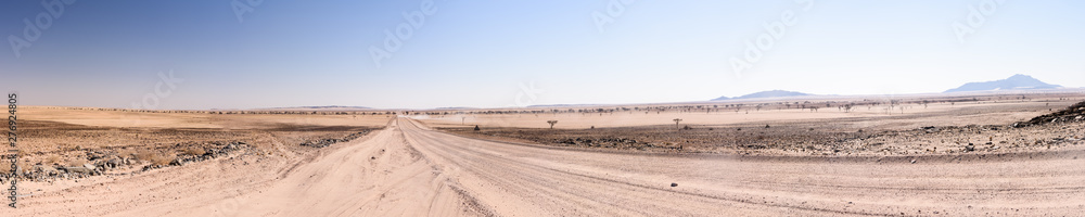 Long gravel dirt road with a distant car leaving a dust trail in Central Namibia Long gravel dirt road with a distant car leaving a dust trail in Central Namibia