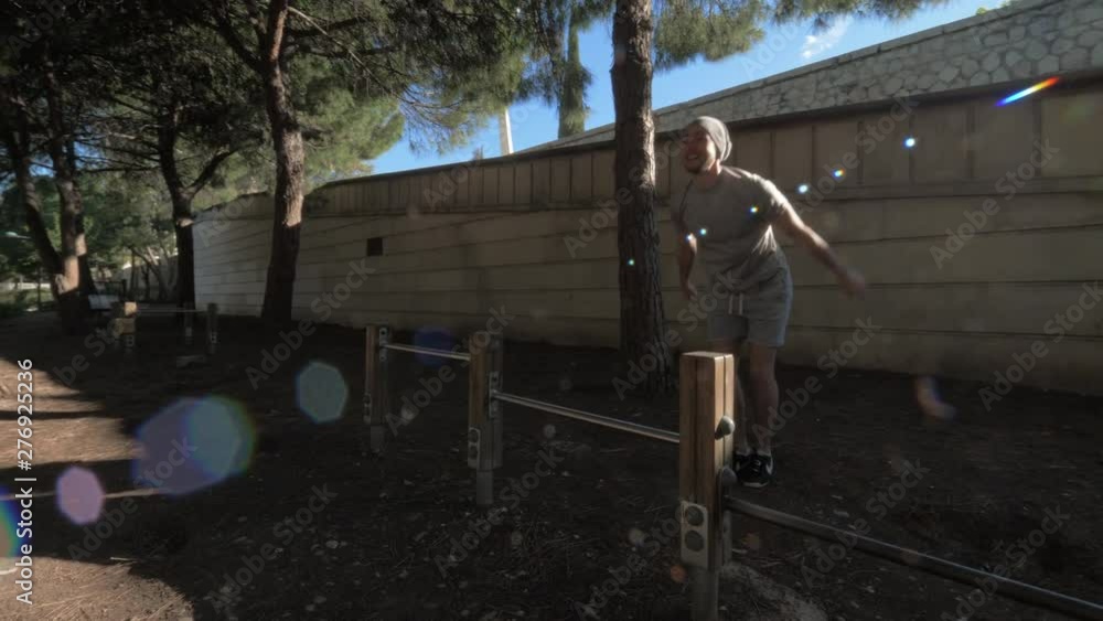 A guy in a grey T shirt and cap is doing push ups in a green sunny yard. He is pushing off the metal crossbar in front of him A guy in a grey T shirt and cap is doing push ups in a green sunny yard. He is pushing off the metal crossbar in front of him