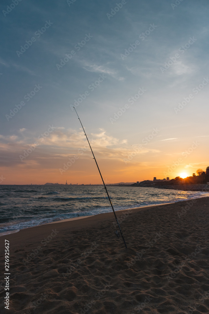Fishing rod on a beach at sunset, landscape with a city in the
