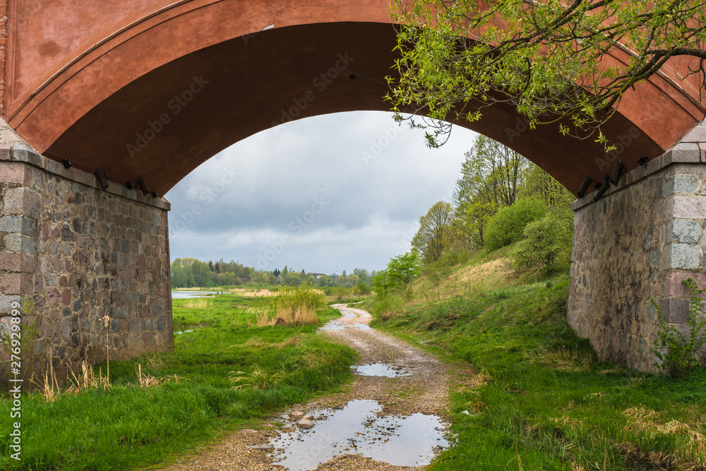 a rural gravel road with puddles after the rain; the path through the bridge arch; a rainy day